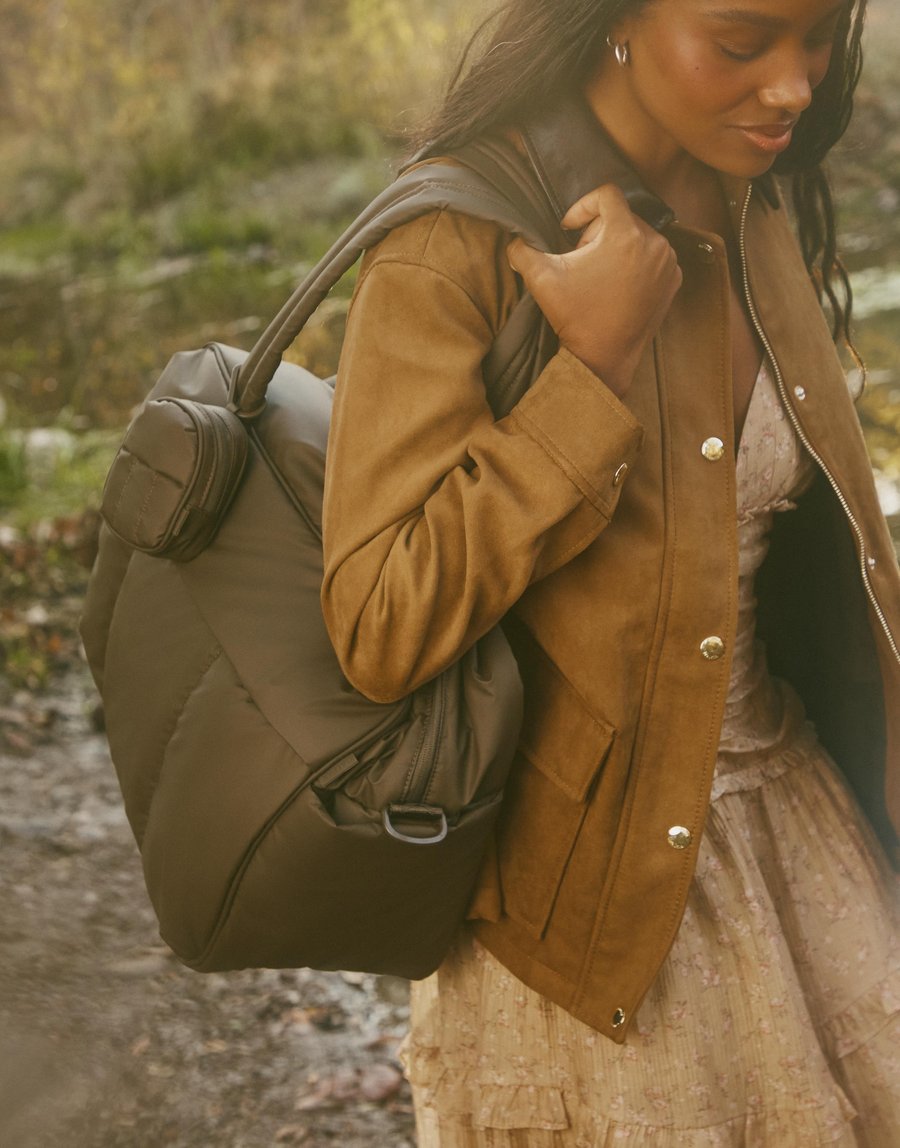 Calpak spot — an olive quilted duffel carried over the shoulder on a wooded trail